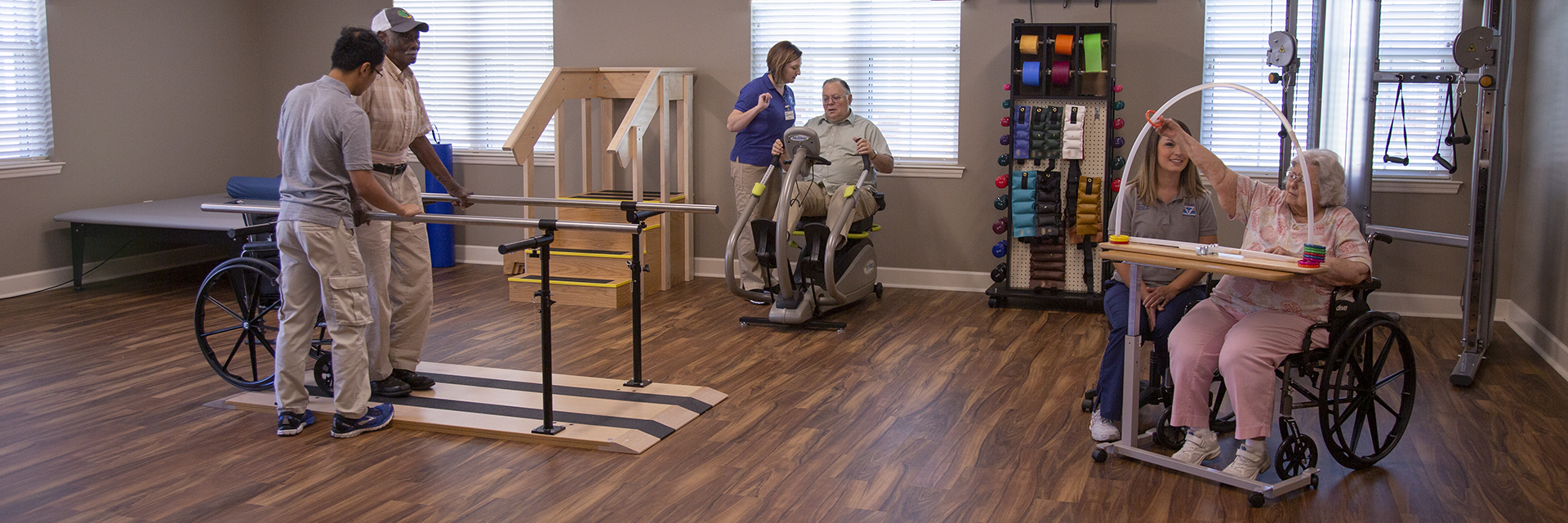 Associates aiding patients at a Rehabilitation Therapy Center with various physical therapy exercises such as walking, peddling a stationary bike, and arm movement exercises